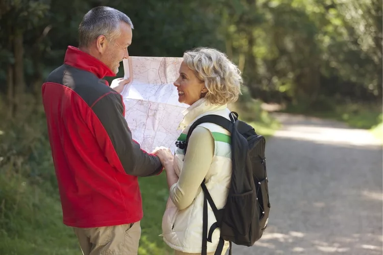 A middle-aged couple, filled with joy, hikes along a scenic trail while simultaneously examining a map.